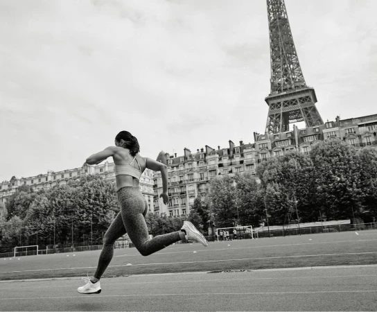 A female athlete running on an outdoor track in Paris with the Eiffel Tower in the background