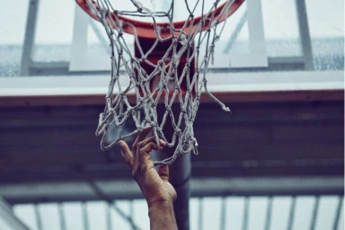 Close-up of a hand touching a frayed basketball net on an outdoor court