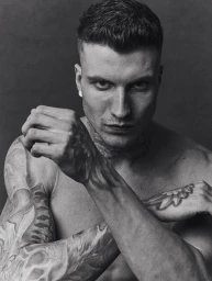 Monochrome portrait of a tattooed man with short hair holding his fists up in a fighting pose