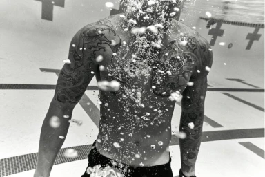 Black and white underwater portrait of a tattooed man swimming in a pool by Coty Tarr.