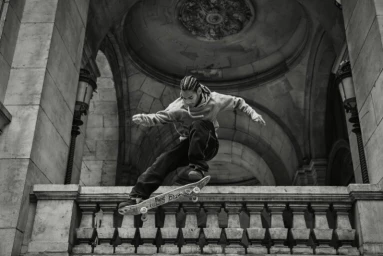 Skateboarder mid-air performing a trick against classical stone architecture by Coty Tarr