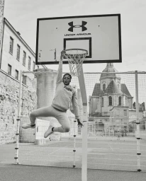 Monochrome action shot of a man dunking a basketball on an outdoor court with a dome building in background by Coty Tarr.