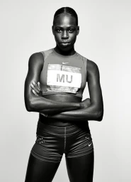 Black female athlete with arms crossed wearing a running crop top and shorts against a white background