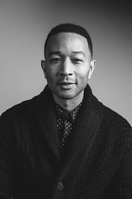 Black and white portrait of a man wearing a cardigan and collared shirt, gazing at the camera against a plain gray background.