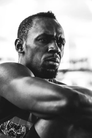 Close-up black and white portrait of Usain Bolt looking intently to the side with muscular arms crossed in the foreground.