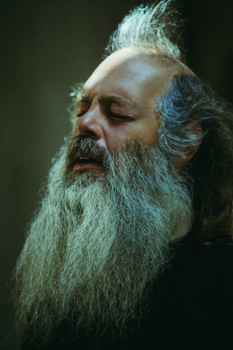 Portrait of a bearded man with his eyes closed in a dimly lit environment, showcasing a contemplative moment in natural light.