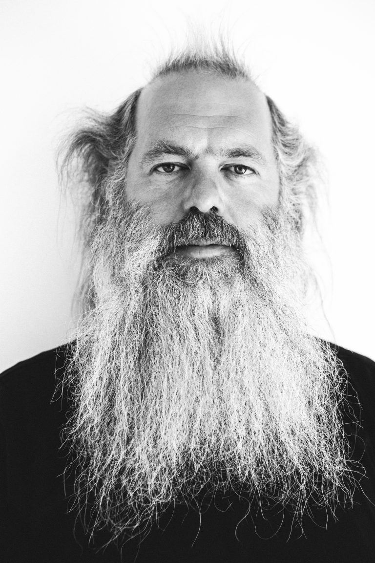 Black and white portrait of an adult male with a long beard against a light background, captured in a close-up, eye-level shot.