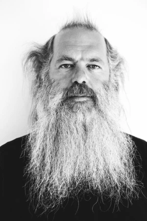 Black and white portrait of an adult male with a long beard against a light background, captured in a close-up, eye-level shot.