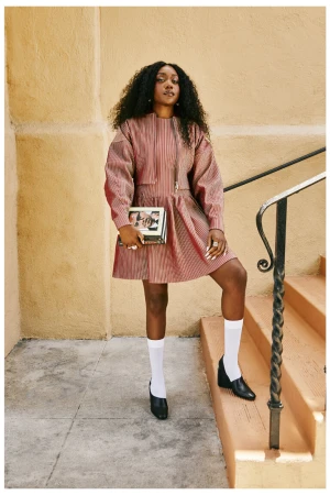Black woman with long curly hair wearing a striped dress and white socks on outdoor stairs.