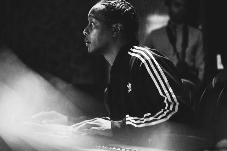 Man in track jacket at mixing board in photo studio, medium shot, black and white photography. Music production with electronic keyboard.