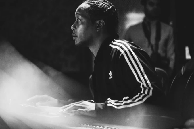 Man in track jacket at mixing board in photo studio, medium shot, black and white photography. Music production with electronic keyboard.