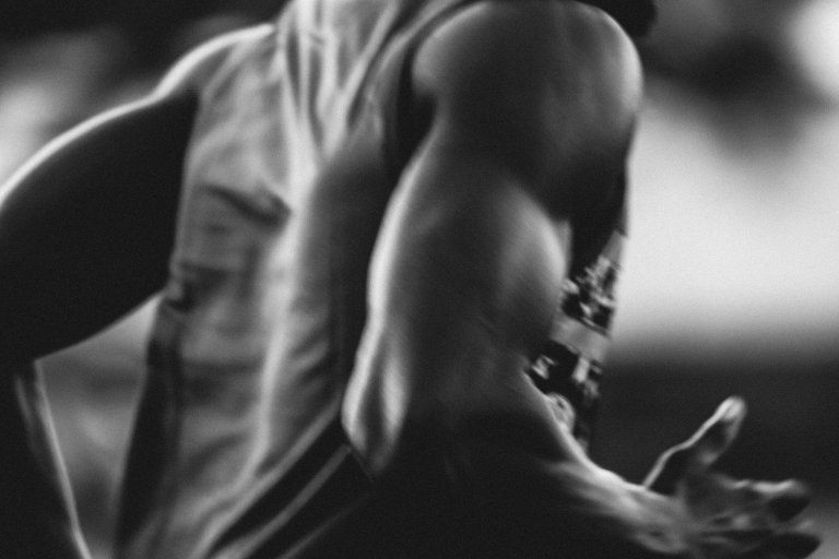 Muscular adult male torso with large bicep, arm and hand in motion, wearing a tank top in a close-up, black and white studio shot.