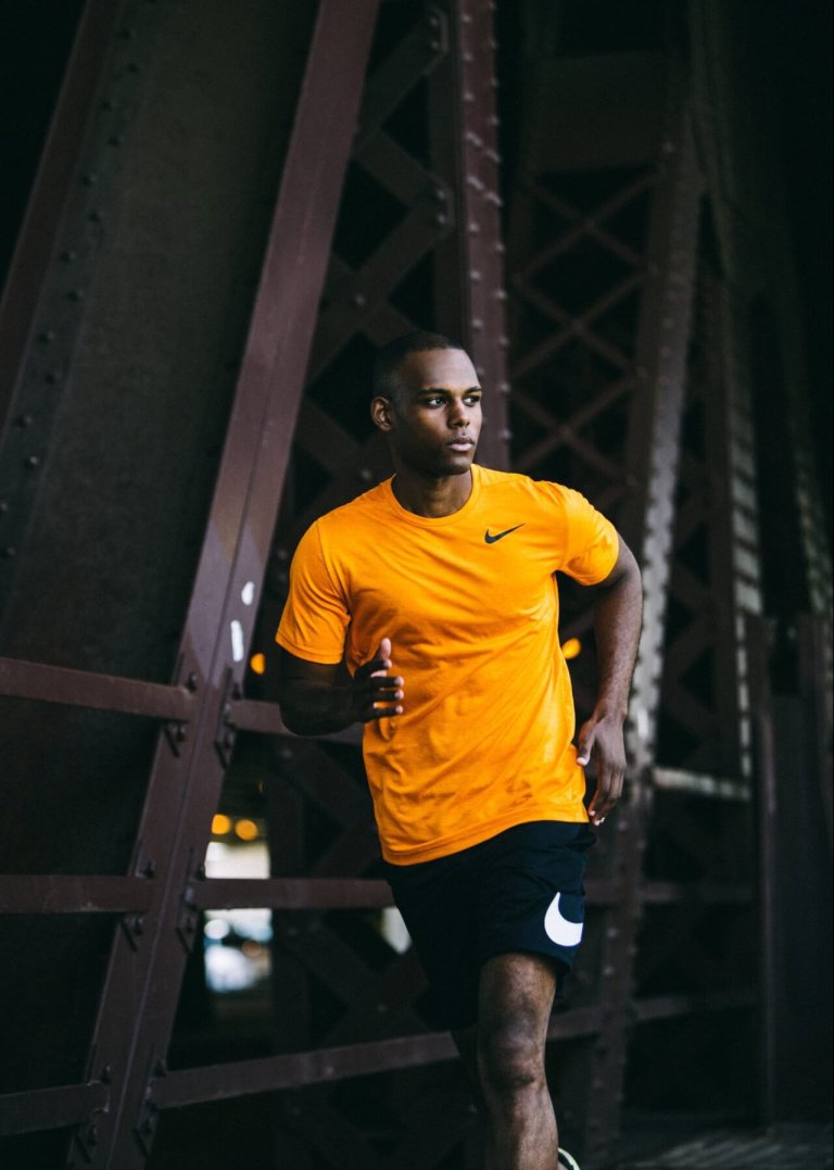 Athletic African-American man in sportswear running outdoors near a metal structure, showcasing fitness and dedication.
