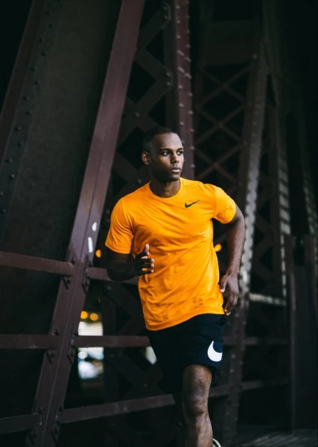 Athletic African-American man in sportswear running outdoors near a metal structure, showcasing fitness and dedication.