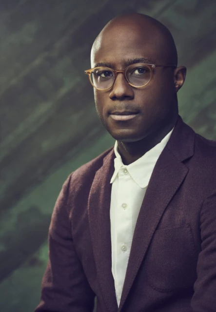 Headshot of a bald, adult male wearing glasses and a suit, set against a mottled green background, captured in a medium portrait shot.