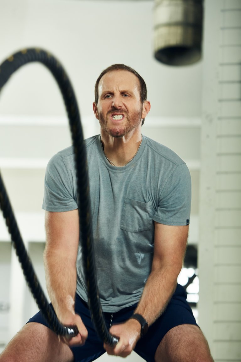 Man exercising with battle ropes in a bright, minimalist gym, showcasing fitness and strength in a high-energy workout.