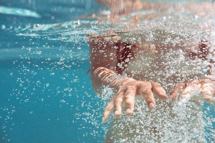 Underwater view of a human hand surrounded by bubbles in clear blue water, creating a sense of depth and movement.