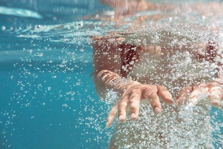 Underwater view of a human hand surrounded by bubbles in clear blue water, creating a sense of depth and movement.