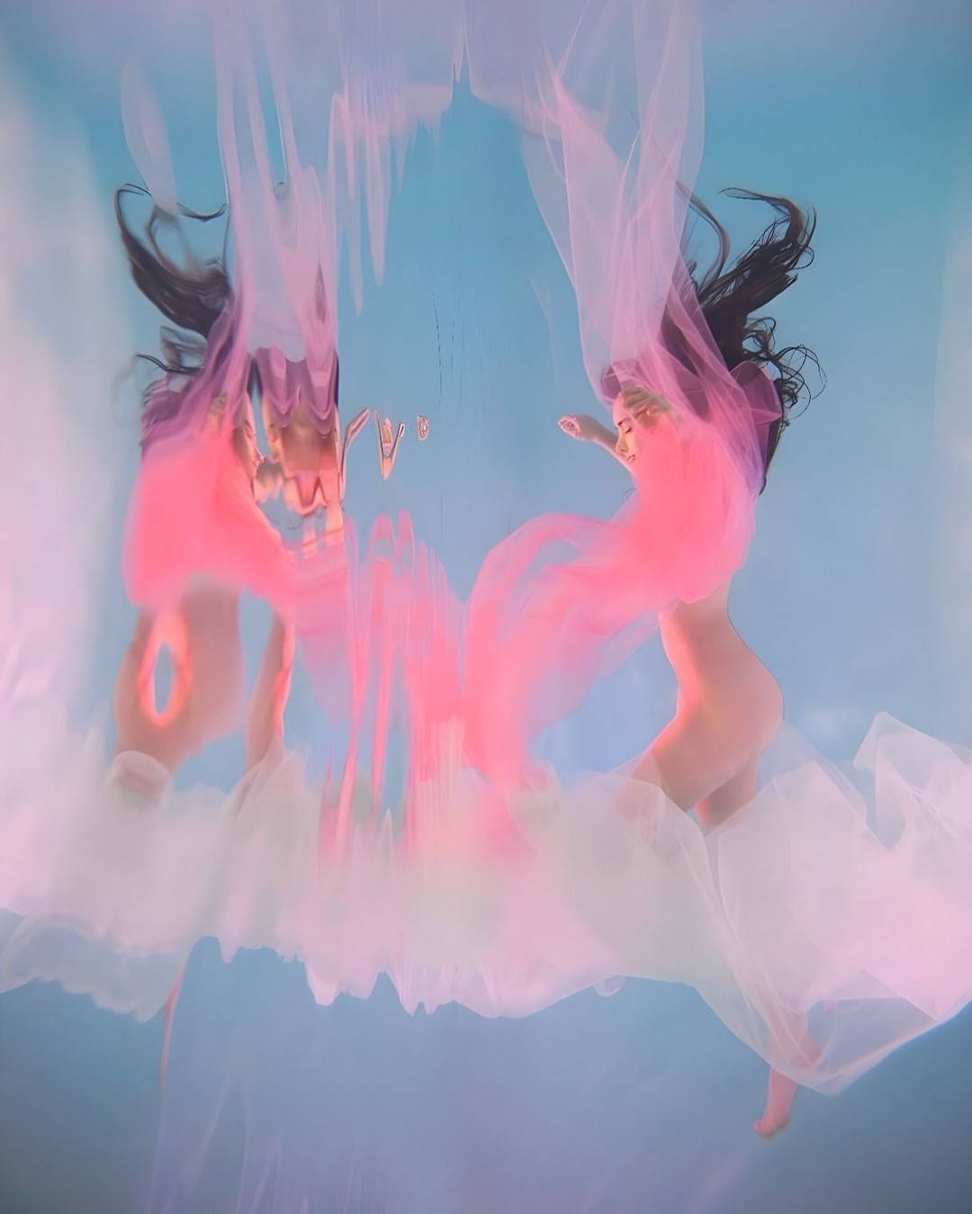 Ethereal underwater portrait of two nude women, draped in pink and white fabric, surrounded by a clear blue aquatic environment.