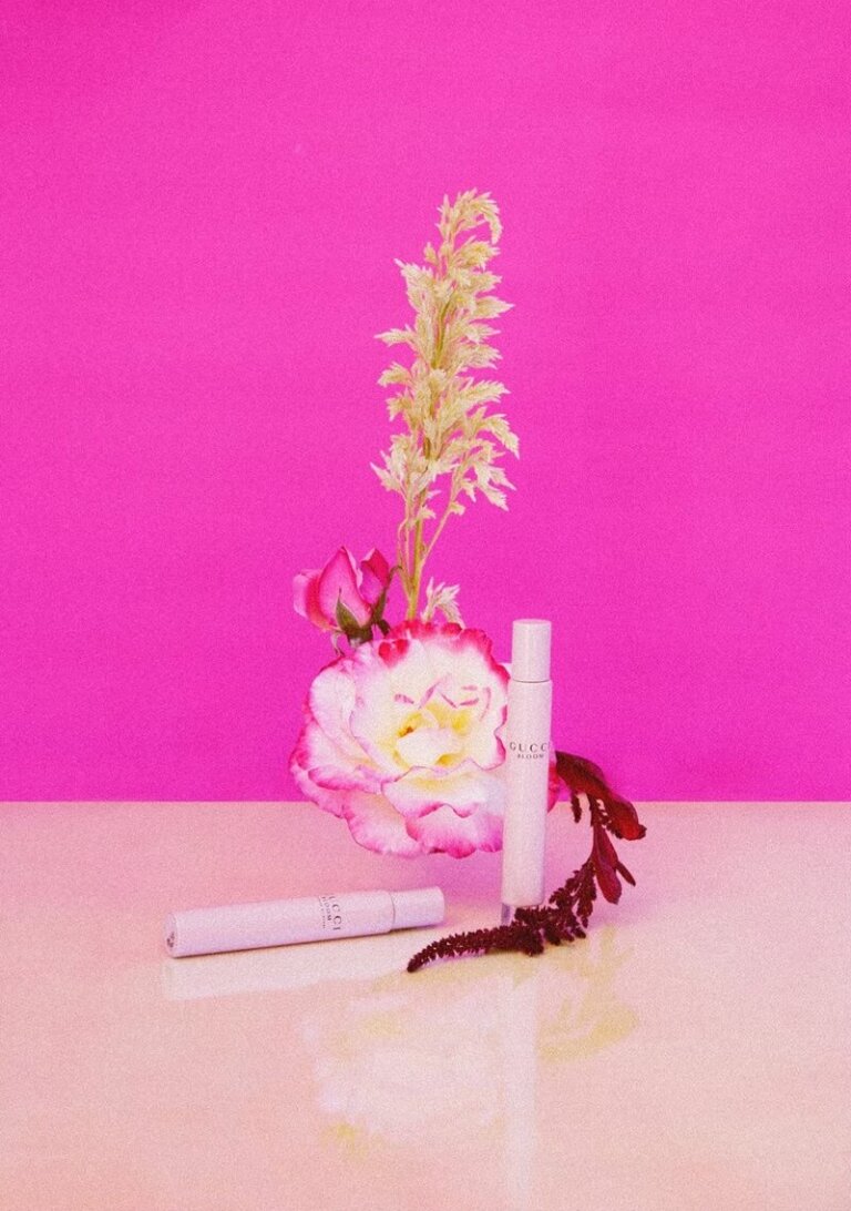 Close-up still life shot of white and pink roses with fragrance bottle product shots against a bright pink backdrop.