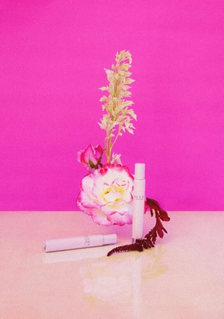 Close-up still life shot of white and pink roses with fragrance bottle product shots against a bright pink backdrop.