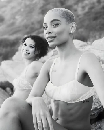 Monochrome portrait of two smiling young women outdoors sitting among natural rocky formations.