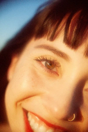 Close-up portrait of a smiling woman with bangs and a nose ring photographed by Nastasia Dusapin.