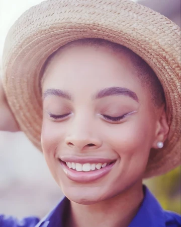 Close-up portrait of a smiling woman wearing a straw hat and blue shirt photographed by Nastasia Dusapin.