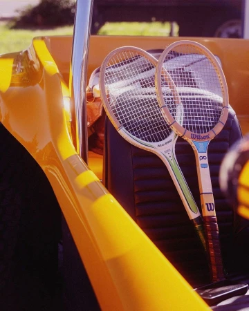 Two Wilson tennis rackets rest inside a yellow vehicle, bathed in sunlight. Close-up captures strings and logos against the dark interior.