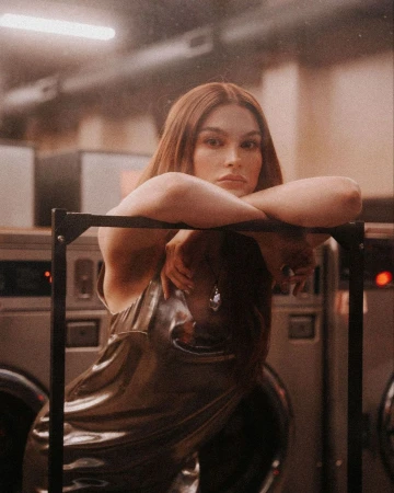 Woman with long reddish-brown hair leaning over a metal rack inside a laundromat