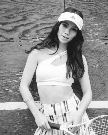 Monochrome portrait of a young woman wearing a visor and athletic crop top holding a tennis racket