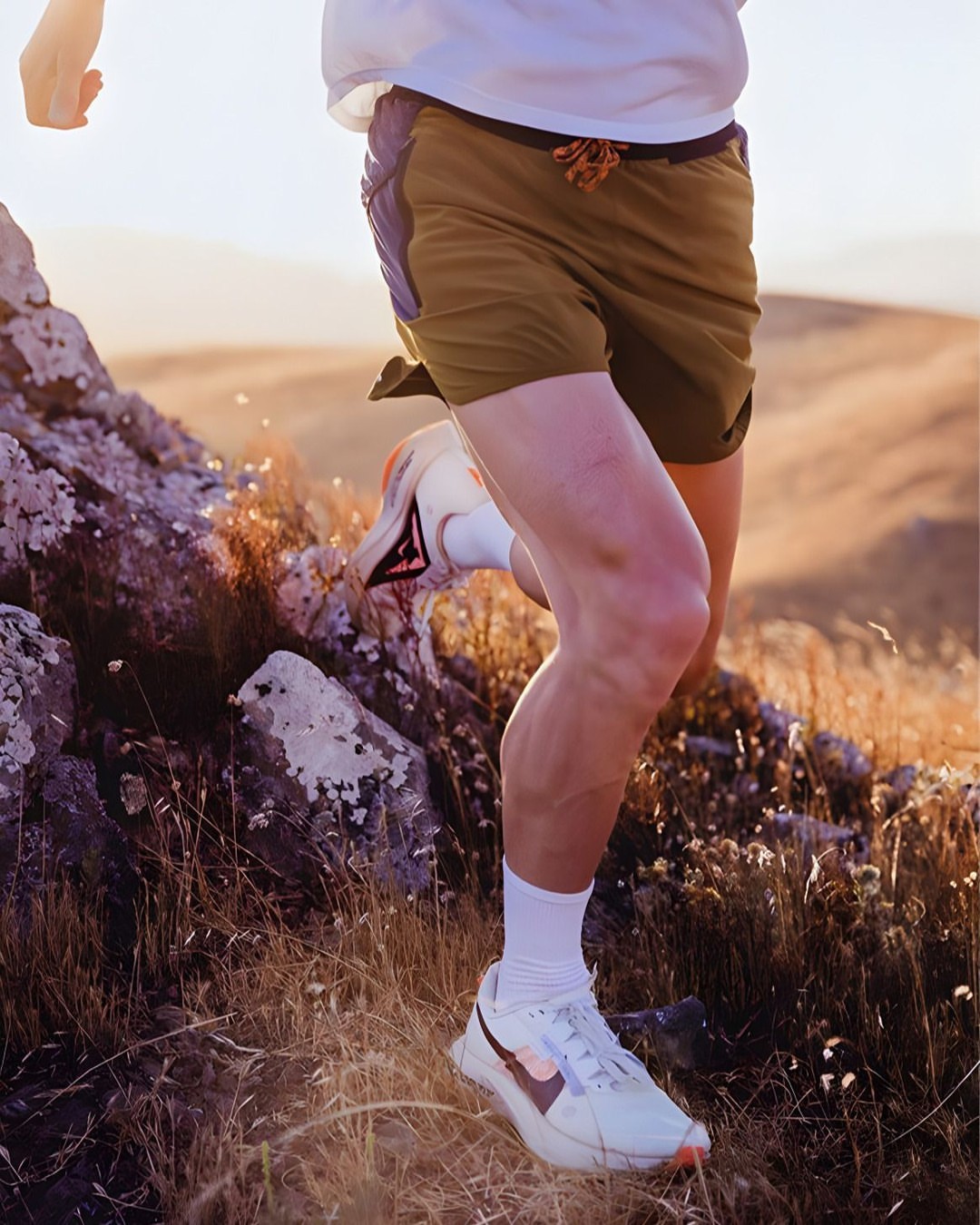 A person is running uphill on a trail with a rocky landscape and golden light illuminating the scene, with emphasis on athletic activity.