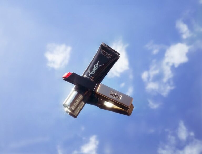 Floating YSL lipsticks and Top Secrets primer against a blue sky backdrop. Beauty still life with cosmetic product photography.