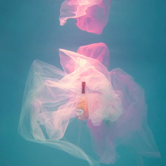A bottle floats underwater amidst transparent plastic bags, creating a surreal and ethereal scene with soft, diffused lighting and gentle hues.