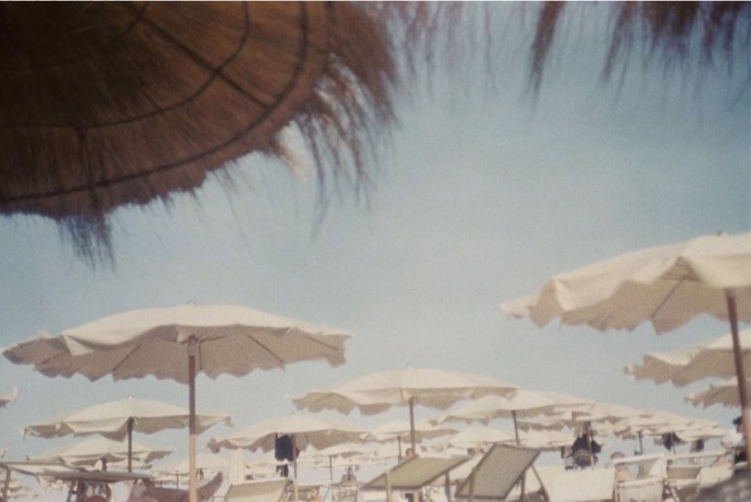 Beach umbrellas and chairs on a crowded beach under a sunny sky, creating a relaxing summer vacation scene.
