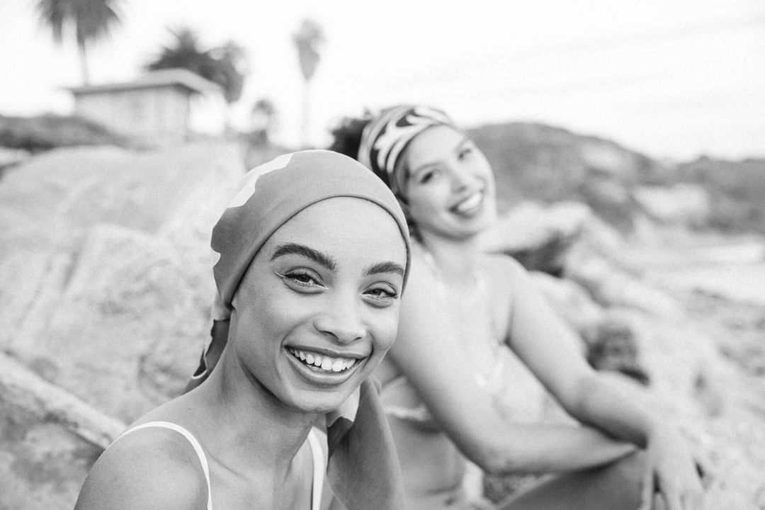 Two smiling women wearing headscarves outdoors near rocky terrain, photographed by Nastasia Dusapin.