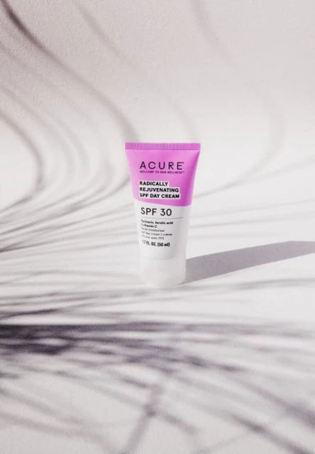 Acure SPF 30 day cream in pink and white tube on white backdrop with leaf shadows, ideal for beauty and skincare product shots.