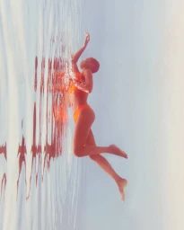Woman with short hair in an orange bikini floating in water by photographer Nastasia Dusapin
