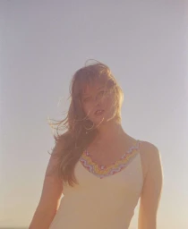 Woman with long blonde hair wearing a cream dress with patterned neckline against a clear sky
