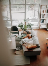 High-angle shot of a couple relaxing on a grey sofa in a living room, holding a remote control