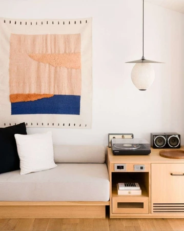 Modern minimalist living room featuring a light wood daybed, a textured wall hanging, and a turntable console by Peter Bohler