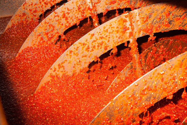 Close-up of red sauce being processed by a metal auger, capturing the food production process with vibrant color and texture.
