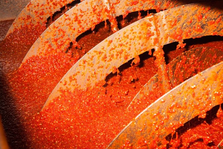 Close-up of red sauce being processed by a metal auger, capturing the food production process with vibrant color and texture.
