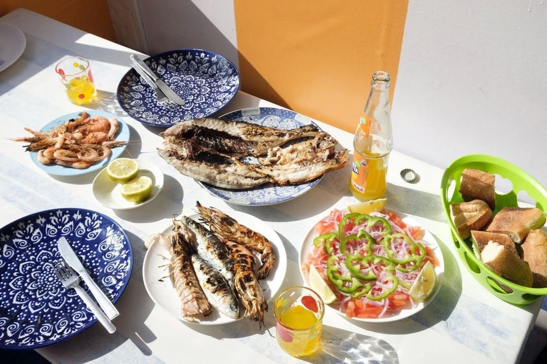 Overhead shot of a table with grilled fish, shrimp, salad, bread, and orange soda in natural lighting, perfect for food and travel content.