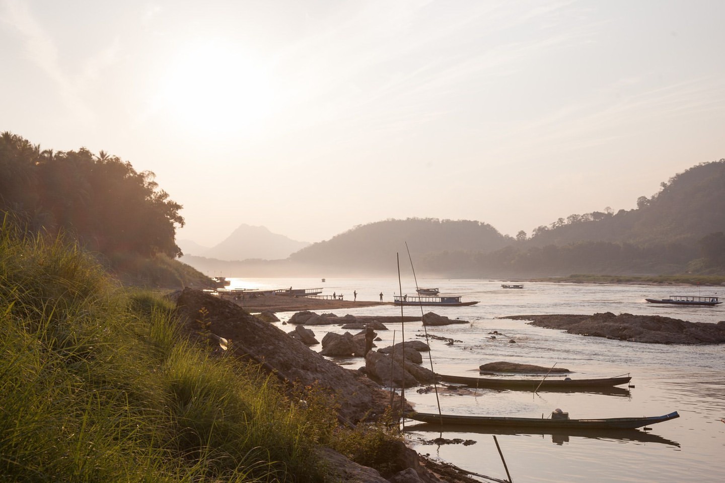 Tranquil scene of several boats on a wide river in a mountainous landscape, captured during daytime under soft, diffused lighting.