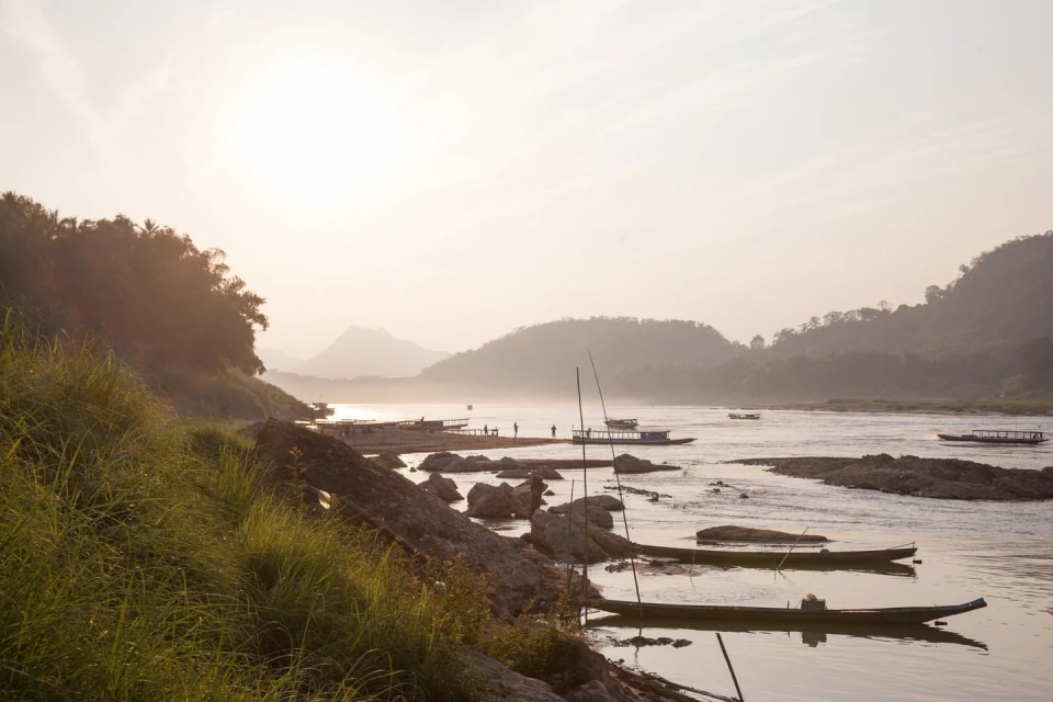 Tranquil scene of several boats on a wide river in a mountainous landscape, captured during daytime under soft, diffused lighting.