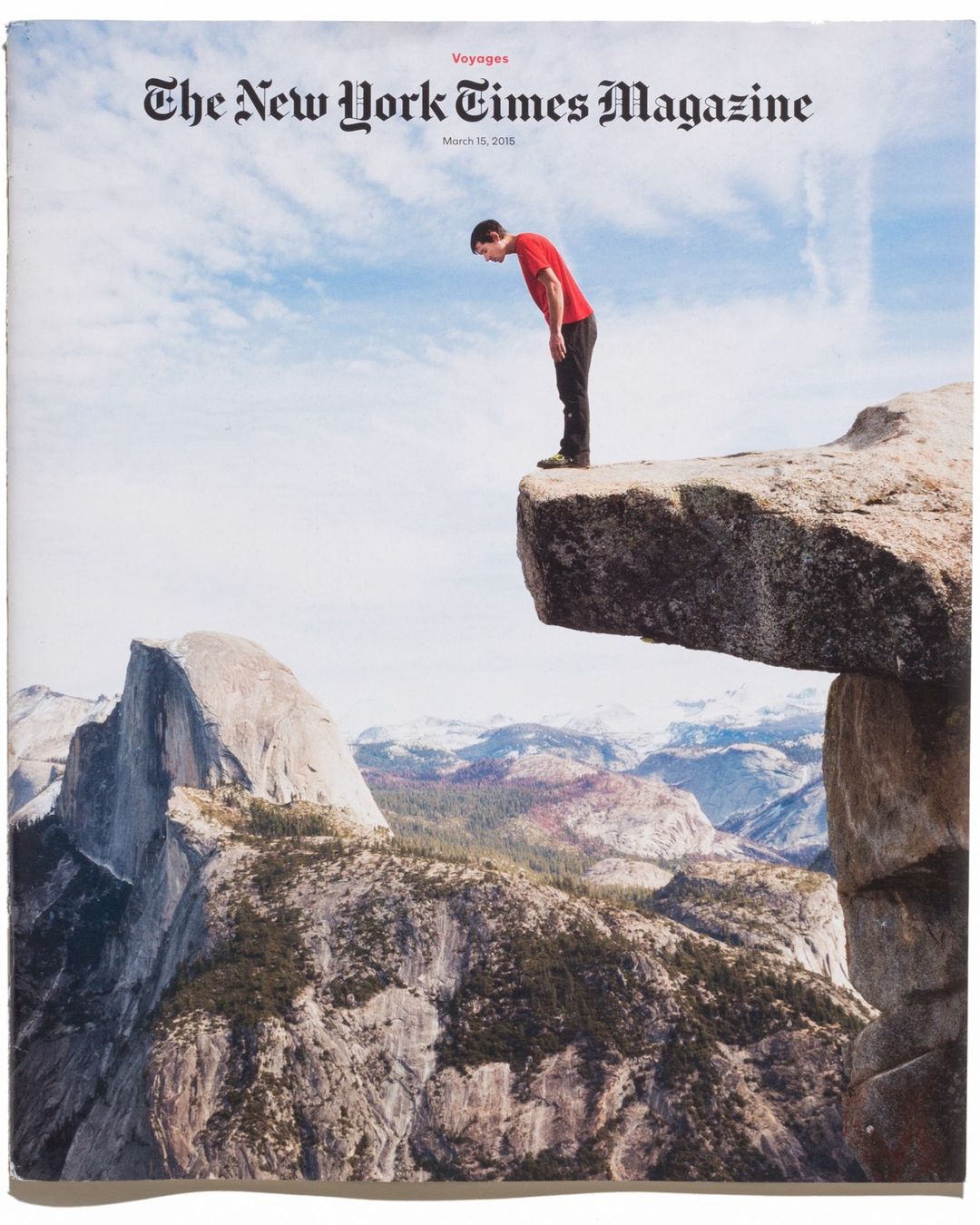 Magazine cover featuring a man standing on a rock cliff edge overlooking a mountain range against a partly cloudy sky, cover art.