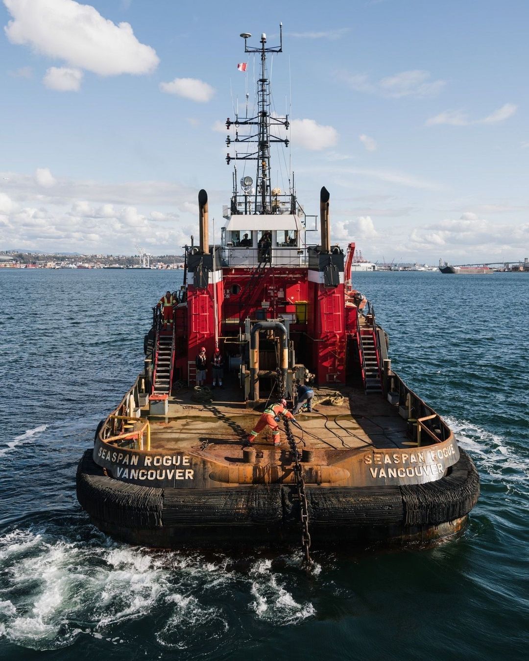 Tugboat underway on the water with blue sky and distant shoreline in the background. The name SEASPAN ROGUE is printed on the boat.