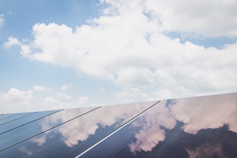 A close-up of solar panels reflecting a blue sky with puffy white clouds, promoting clean energy and sustainable technology.