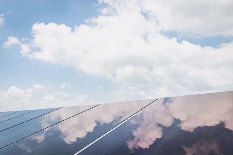 A close-up of solar panels reflecting a blue sky with puffy white clouds, promoting clean energy and sustainable technology.